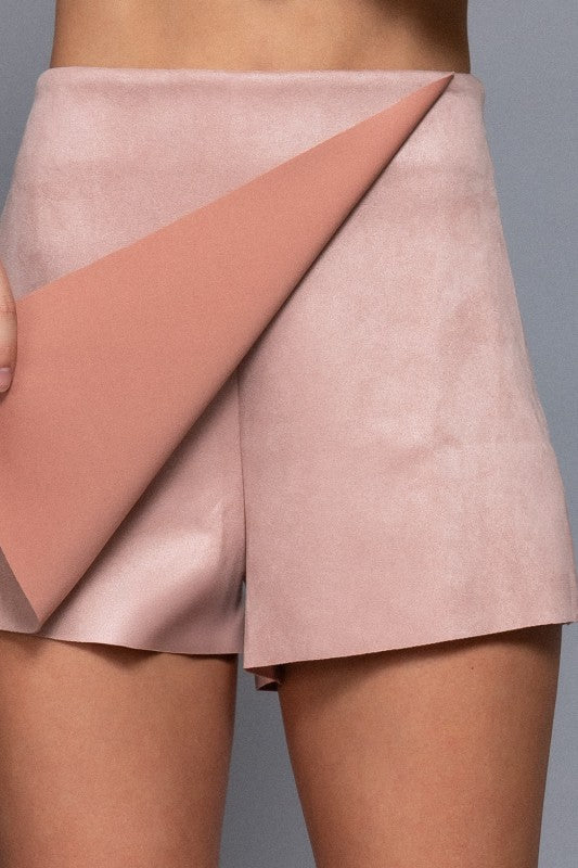 Close-up of a person wearing a pink and peach color-blocked skirt against a gray background.