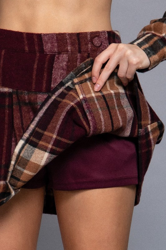 Person wearing a plaid shirt over a burgundy skirt on a gray background