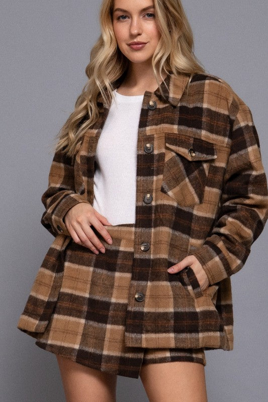 Woman wearing a brown plaid jacket over a white shirt on a gray background