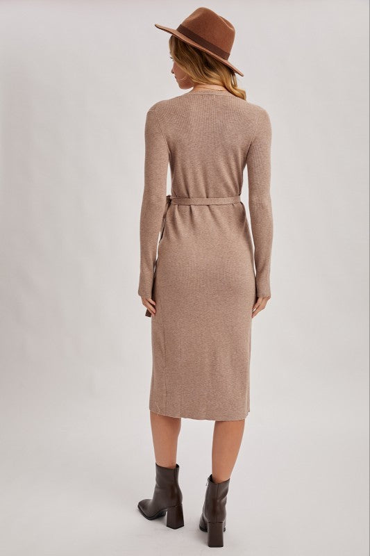 Woman wearing a beige ribbed dress with a belt, brown hat, and gray boots on a white background
