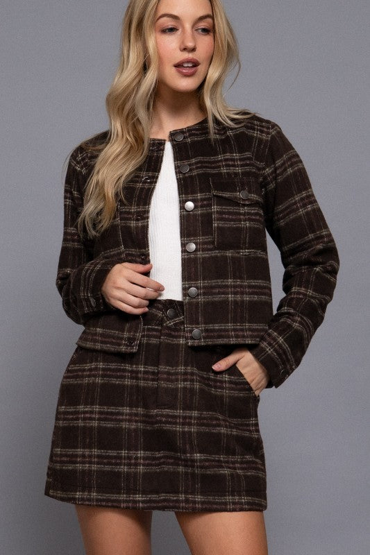 Woman wearing a brown plaid jacket and skirt set against a gray background
