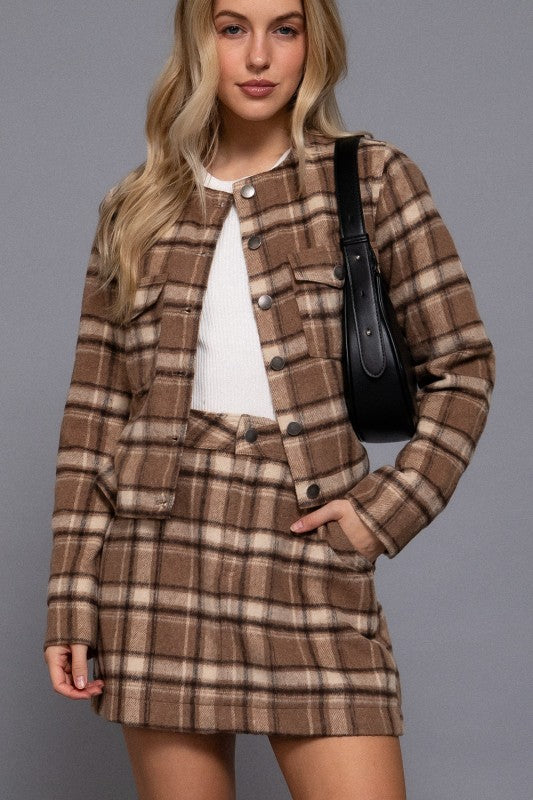 Woman wearing a brown plaid suit with a black handbag on a gray background