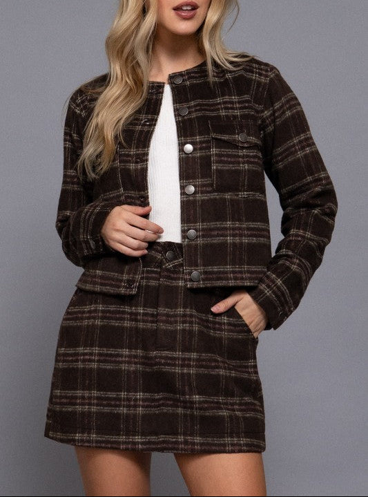 Woman wearing a brown plaid jacket and skirt set against a gray background