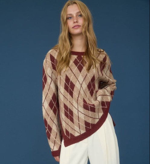 Person wearing a patterned sweater and white pants against a blue background