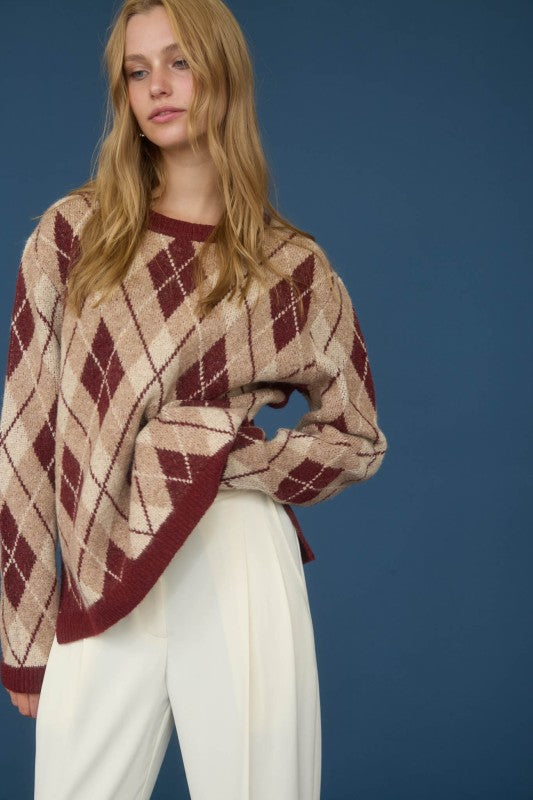 Woman wearing a patterned sweater and white pants against a blue background