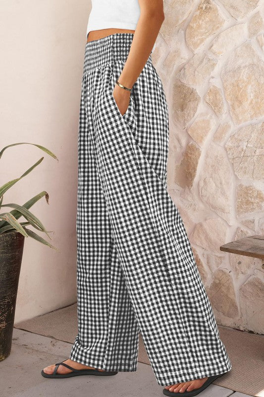 Person wearing black and white checkered pants standing against a stone wall.