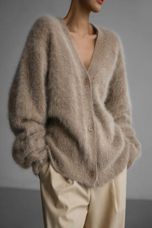 Person wearing a fluffy beige cardigan against a gray background