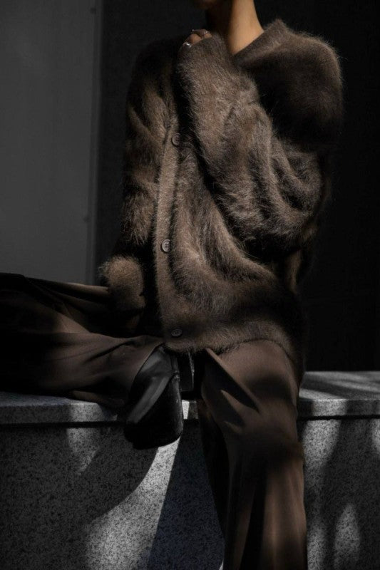 Person wearing a brown fur coat and pants sitting on a concrete surface.