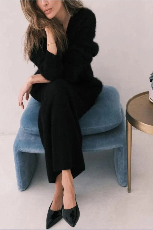 Woman in black outfit sitting on a blue stool with a white background