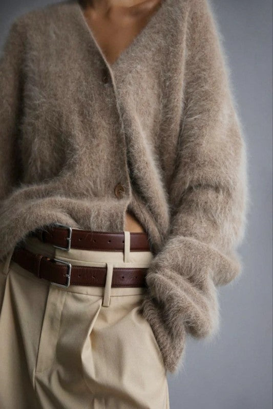 Person wearing a brown fuzzy sweater and beige pants with a belt, on a gray background