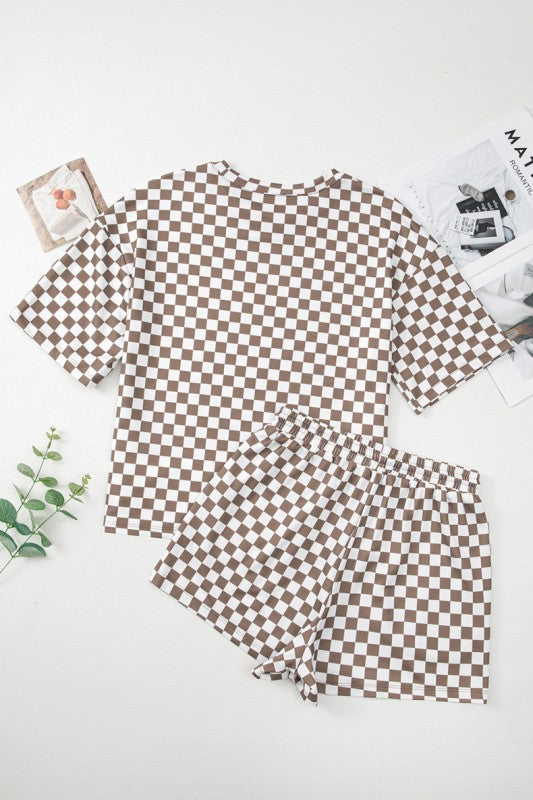 Brown checkered pajama set on a white surface with magazines and a plant.