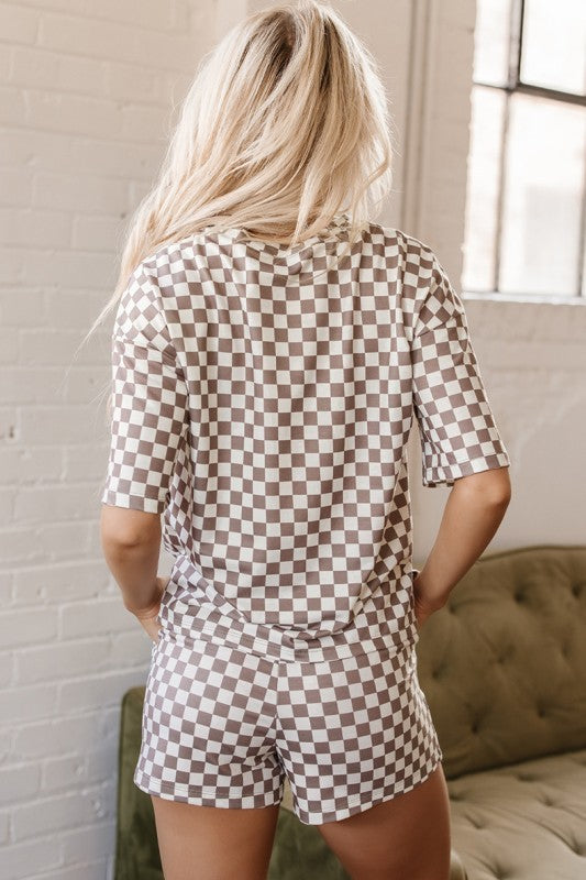 Person wearing a checkered romper in a room with a window and couch.