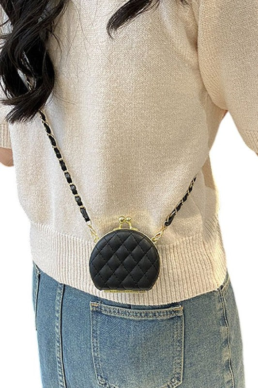 Person wearing a beige sweater and blue jeans with a black quilted handbag.
