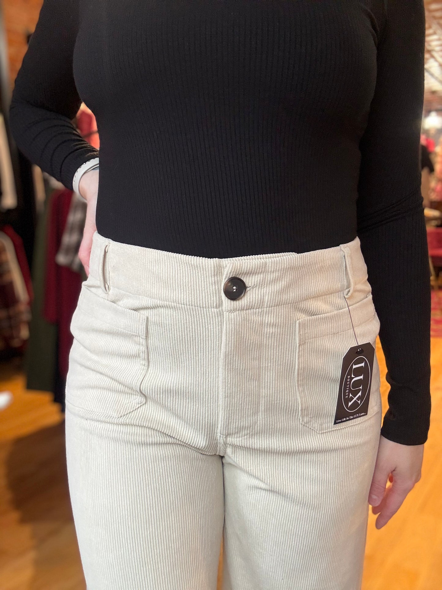 Person wearing light-colored corduroy pants with a black ribbed top, standing indoors.