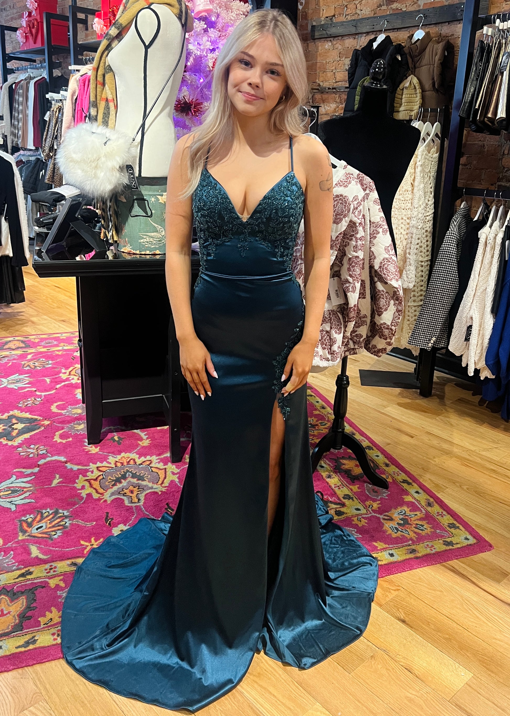 Woman in a blue evening gown standing in a clothing store with racks and mannequins in the background.