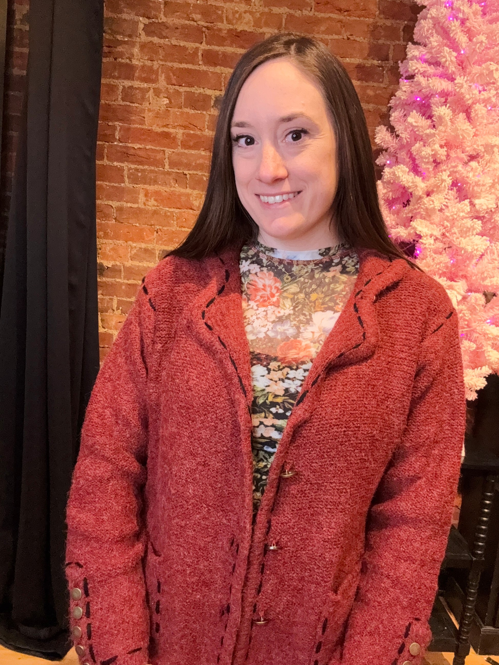 A woman wearing a red blazer with a classic pattern, featuring long sleeves, stitch detailing, lightly padded shoulders, and decorative gold buttons.
