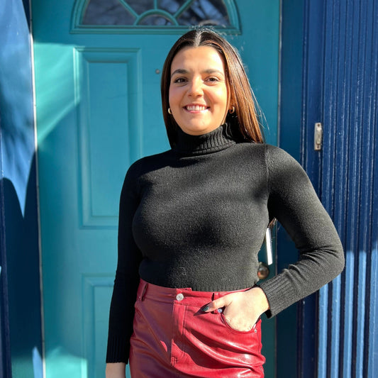 Woman wearing a black turtleneck and red leather skirt standing in front of a blue door.