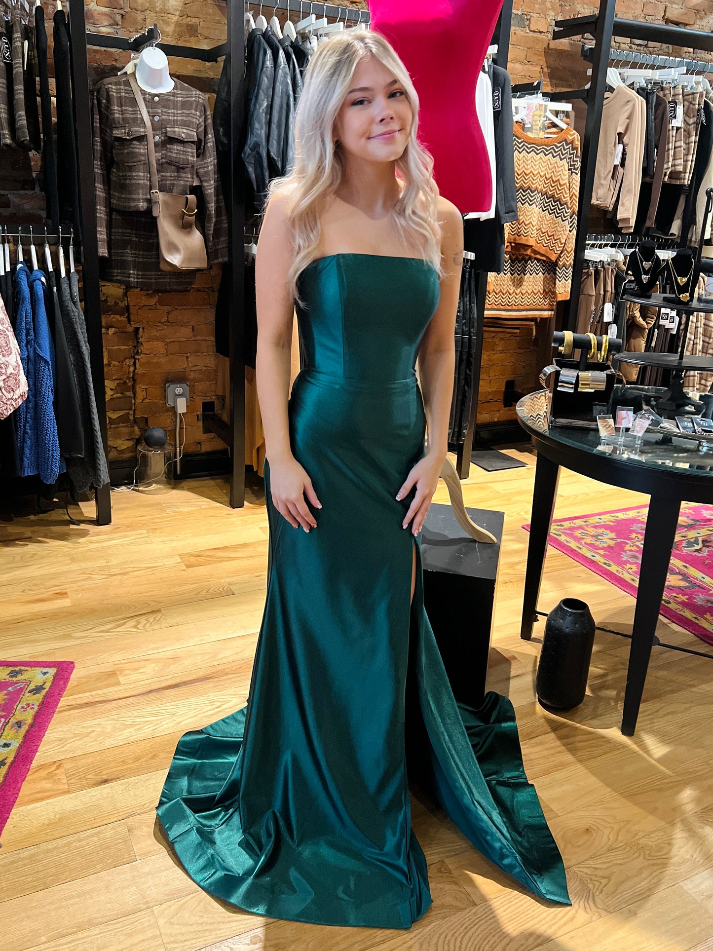 Woman in a teal strapless gown standing in a clothing store.