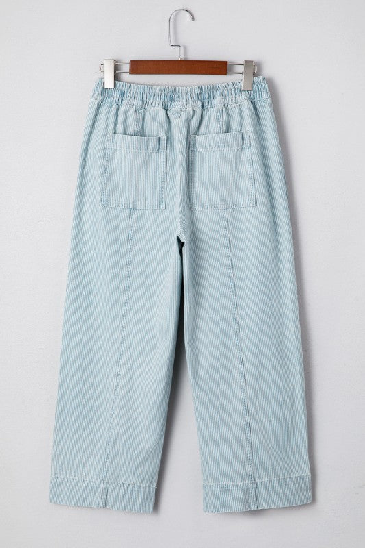 Light blue pants hanging on a wooden hanger against a light gray background