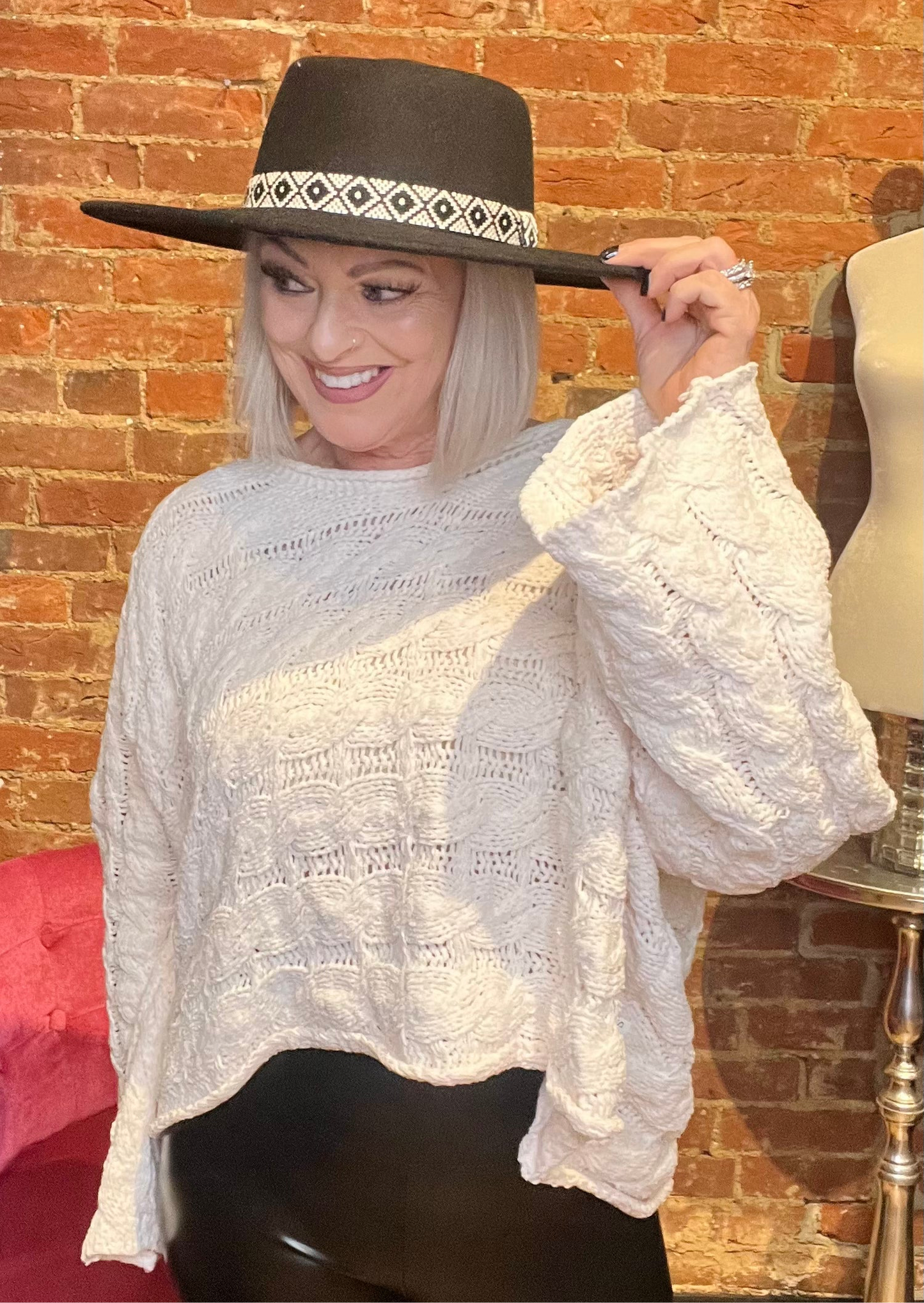 A woman wearing a semi-cropped white sweater with a round neckline and full sleeves. She is also wearing a wide-brimmed hat.