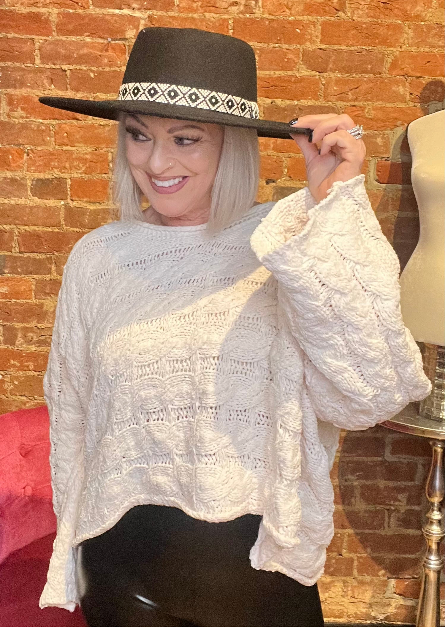 A woman wearing a semi-cropped white sweater with a round neckline and full sleeves. She is also wearing a wide-brimmed hat.