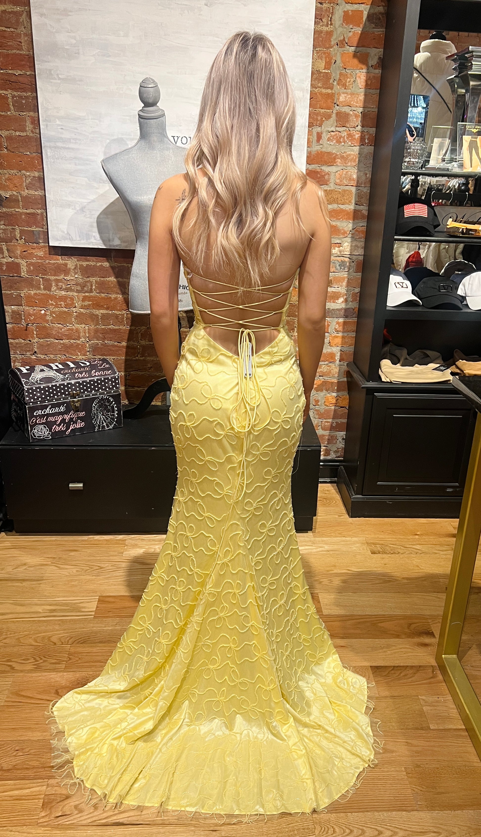 Woman wearing a yellow evening gown with a lace-up back in an indoor setting.
