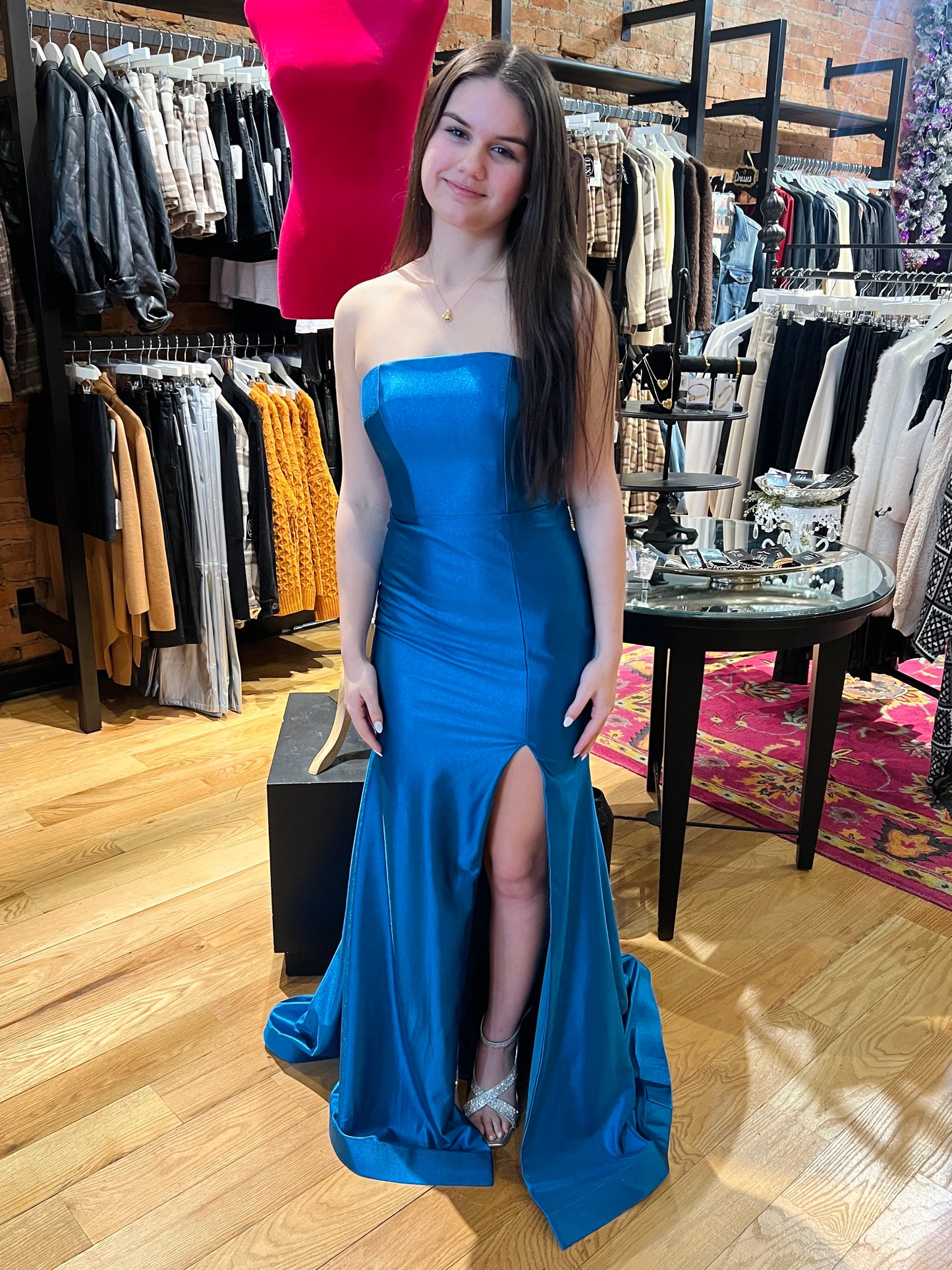 Woman in a blue strapless gown with a slit standing in a clothing store.