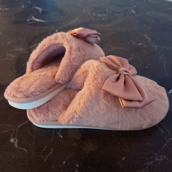Pair of pink fuzzy slippers with bow details on a dark marble surface