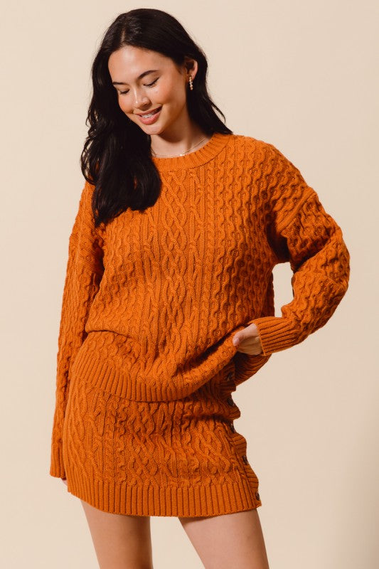 Woman wearing an orange knitted sweater and skirt set against a beige background