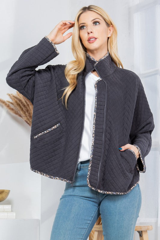 Woman wearing a dark gray quilted jacket with white trim against a light background