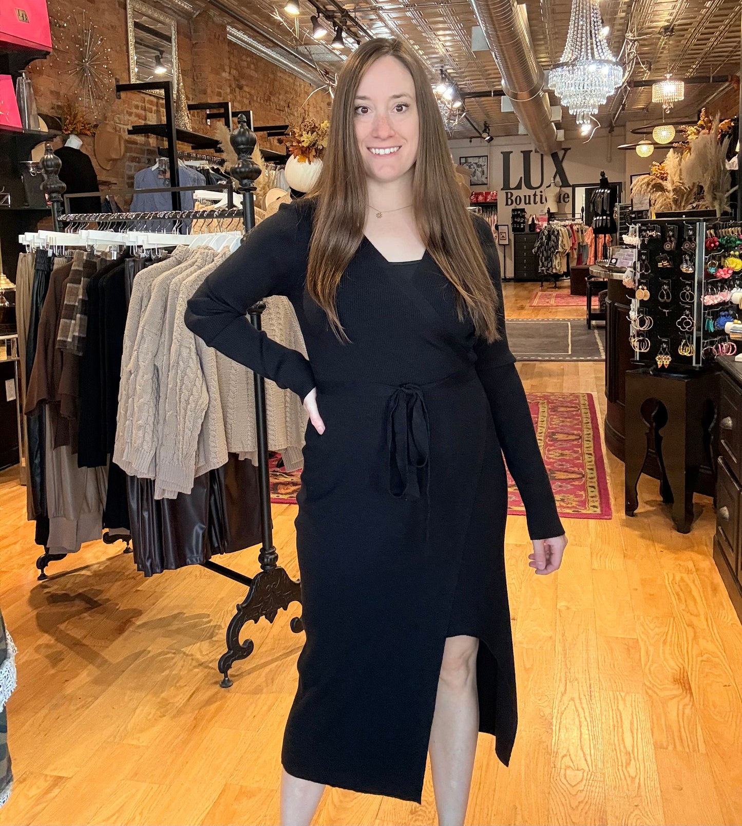 Woman in a black dress standing in a clothing store with racks and displays in the background.