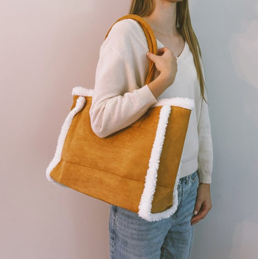 Person holding a mustard yellow tote bag with white trim against a plain background