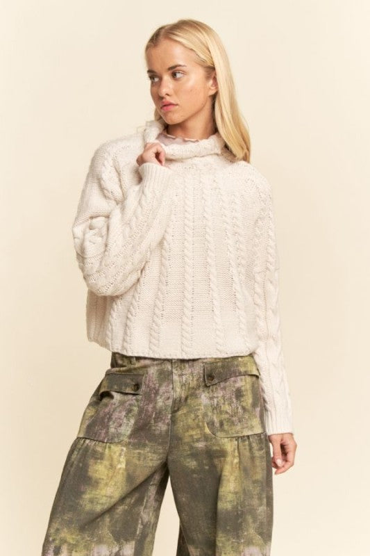 Woman wearing a white cable knit sweater and camouflage pants on a beige background