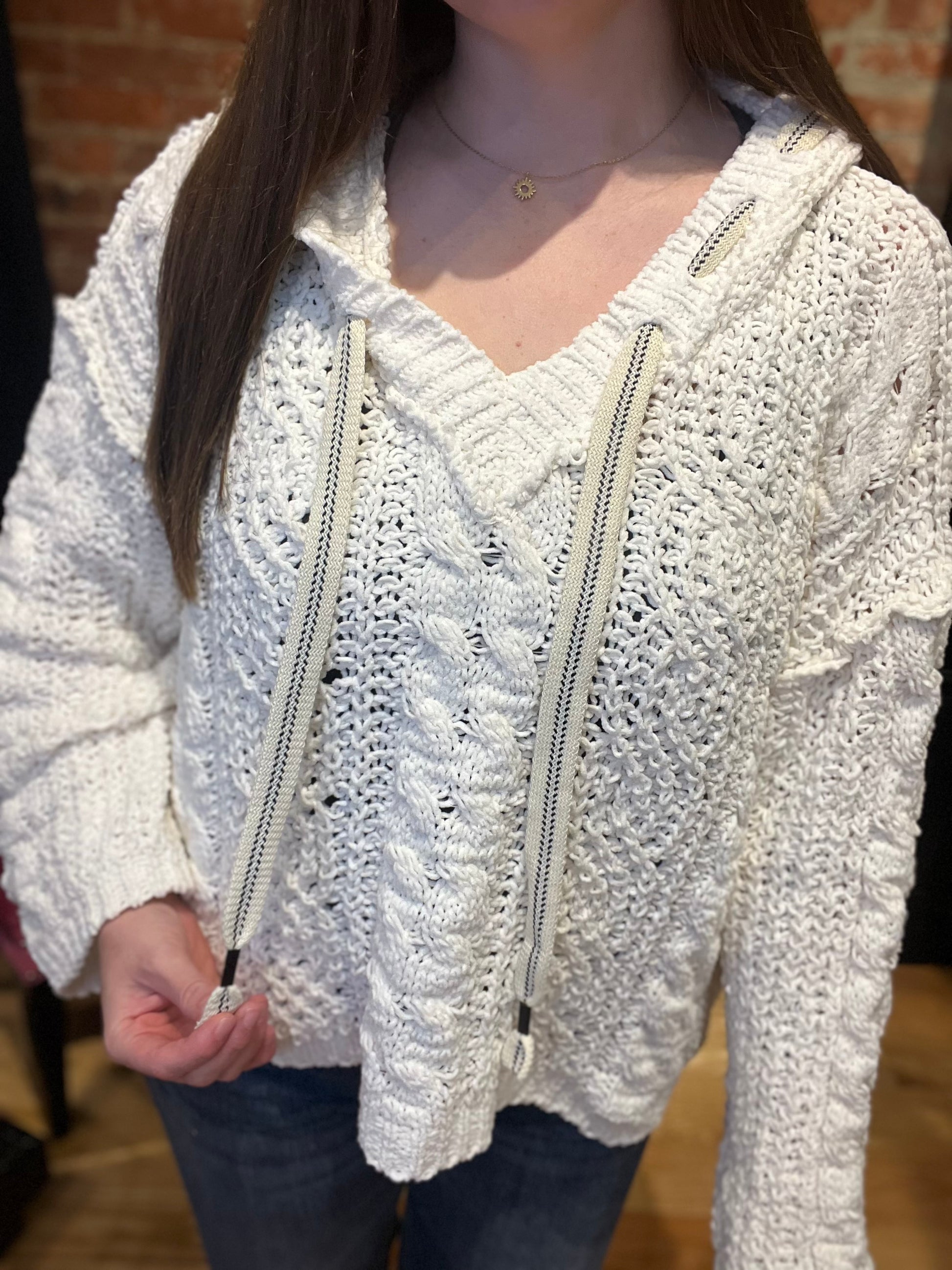 A woman smiling and wearing a white cozy pullover sweater with a v-neckline and long sleeves, paired with jeans.