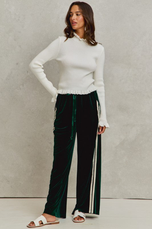 Woman wearing a white sweater and green pants with white stripes against a neutral background