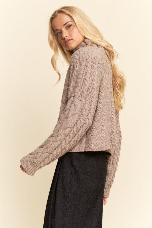 Woman wearing a cable knit sweater against a beige background
