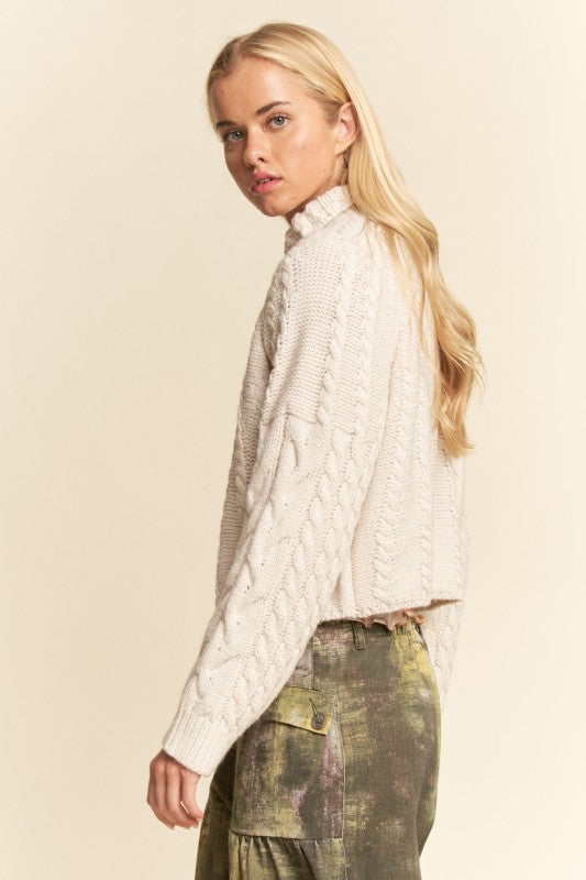 Woman wearing a cream cable knit sweater and green pants on a beige background