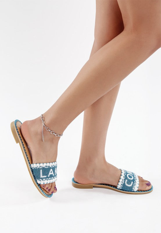 Blue sandals with white embellishments worn by a person on a light gray background