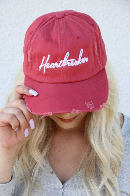 Red cap with 'Heartbreaker' text worn by a person against a white background