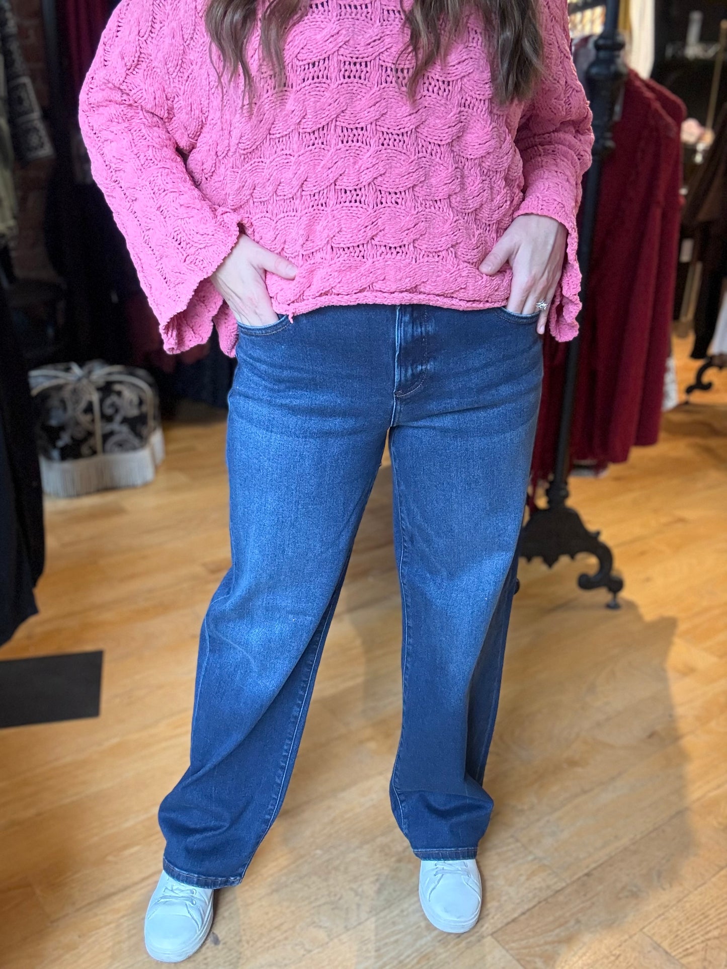 Person wearing a pink knitted sweater and blue jeans in a clothing store.