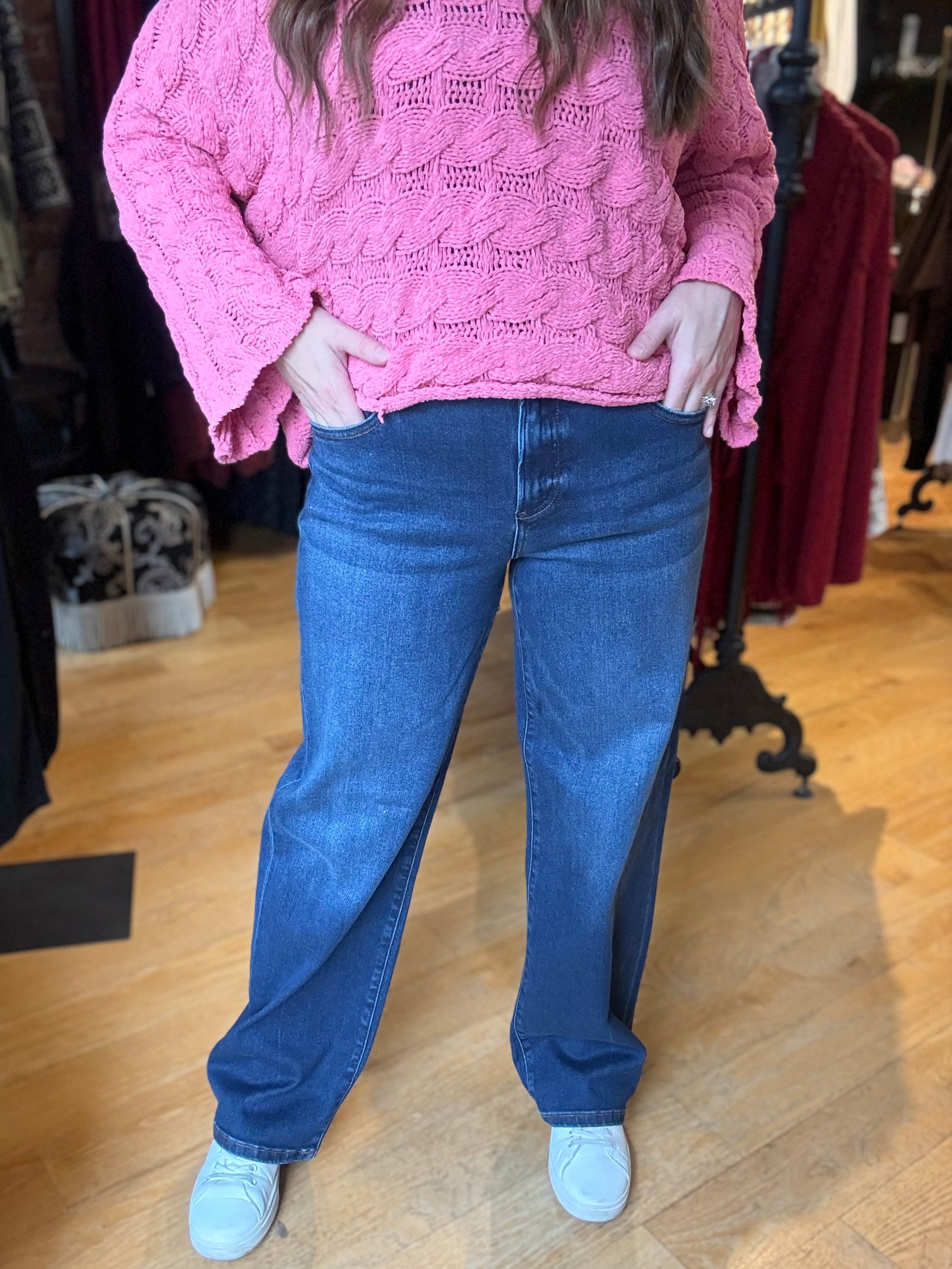 Person wearing a pink knitted sweater and blue jeans in a clothing store.