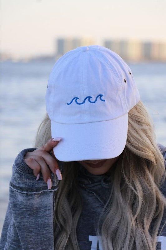 Person wearing a white cap with a blue wave design by a body of water.