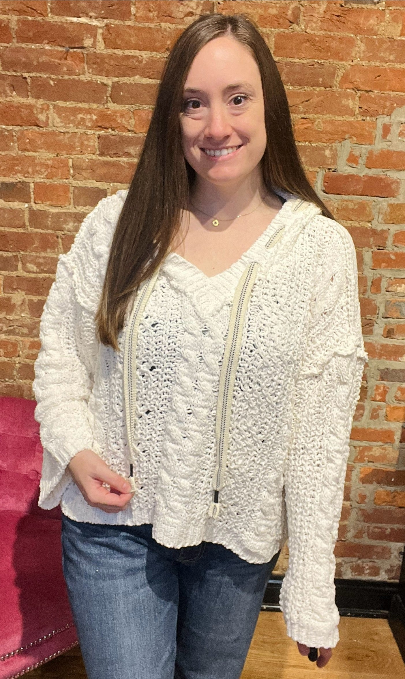 A woman smiling and wearing a white cozy pullover sweater with a v-neckline and long sleeves, paired with jeans.