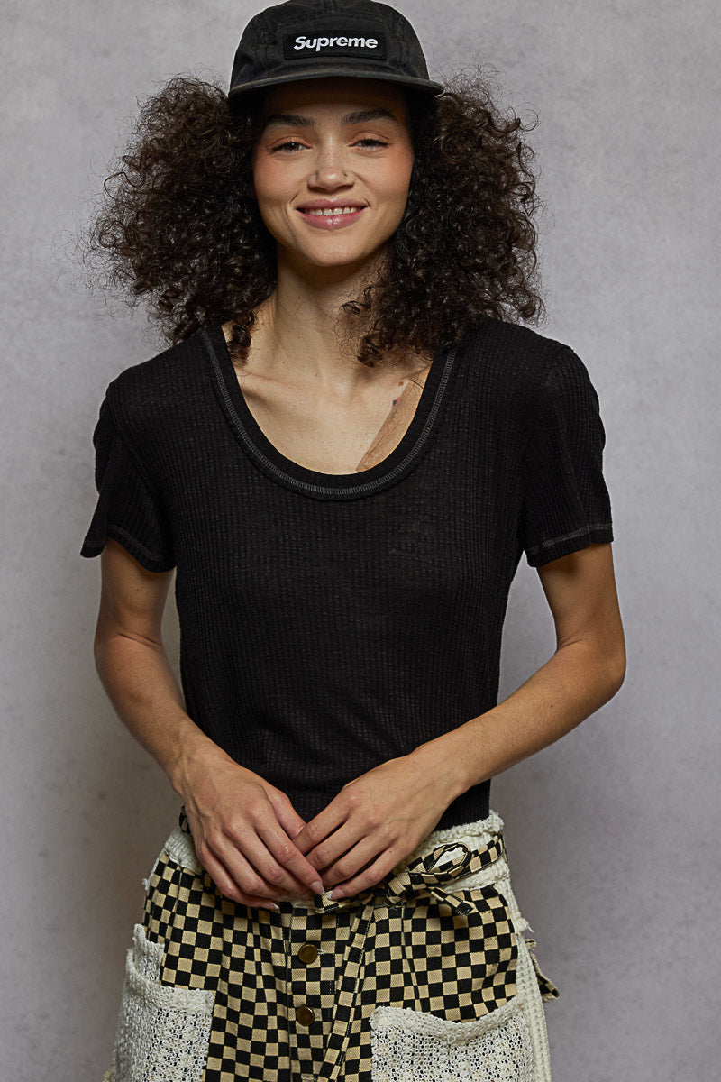 Person wearing a black t-shirt and patterned pants against a plain background