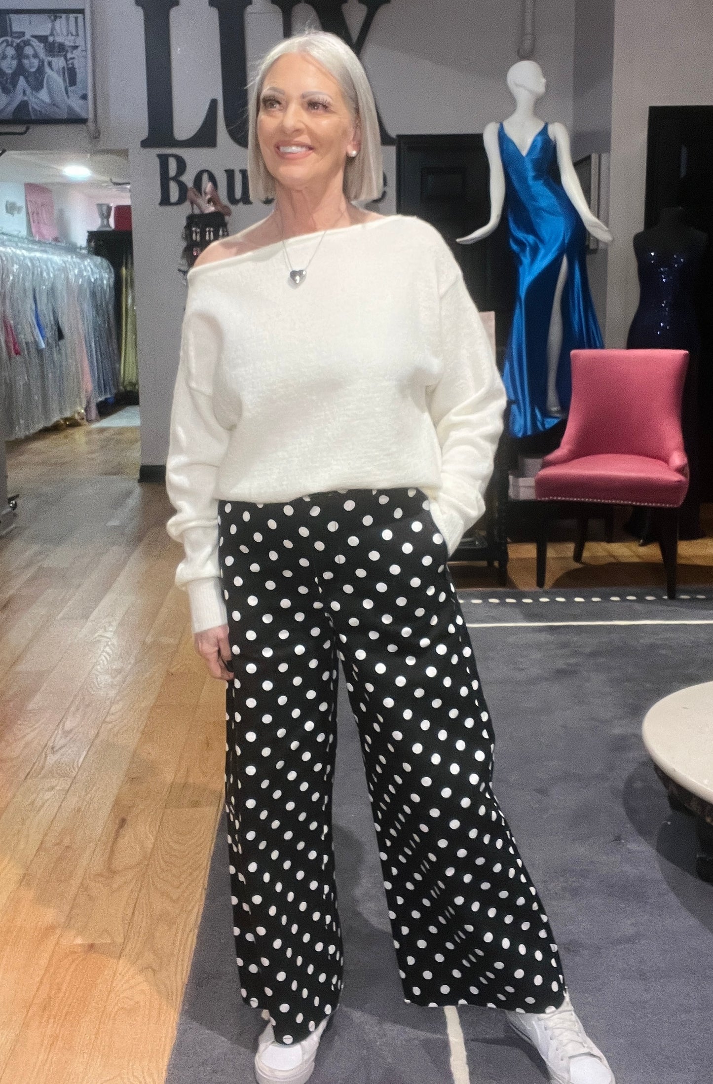Woman wearing a white sweater and black polka dot pants in a store setting.