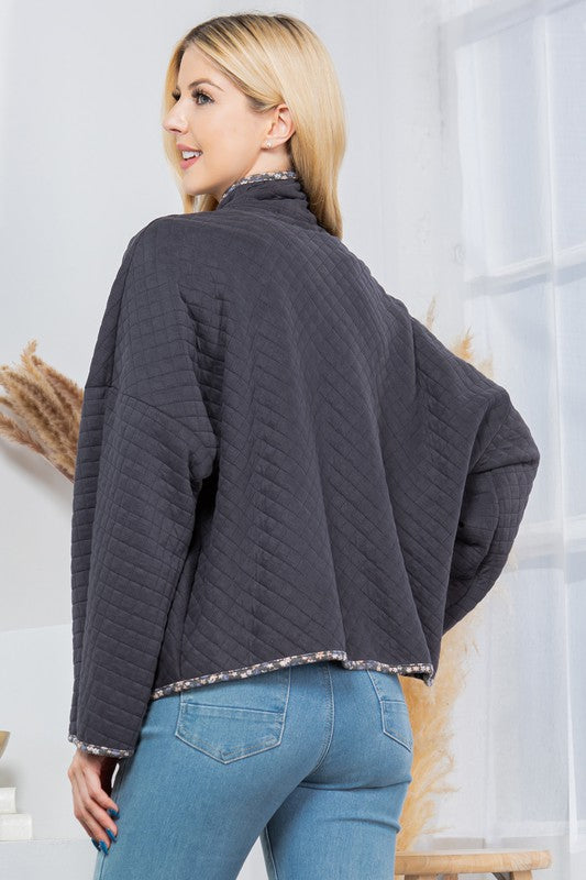 Woman wearing a dark gray quilted jacket and blue jeans indoors.