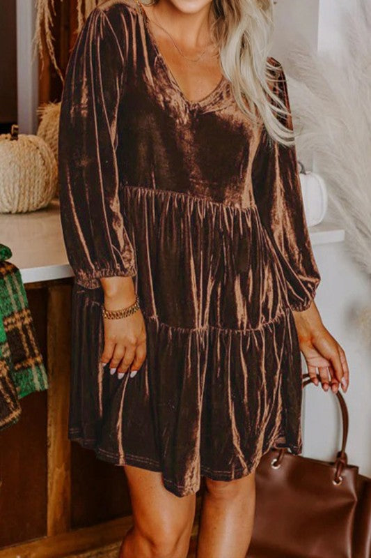 Woman wearing a brown tiered dress holding a brown handbag indoors.