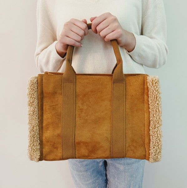 Person holding a brown tote bag with textured handles against a plain background