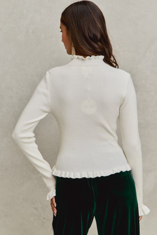 Woman wearing a white ribbed sweater with a ruffled collar against a neutral background