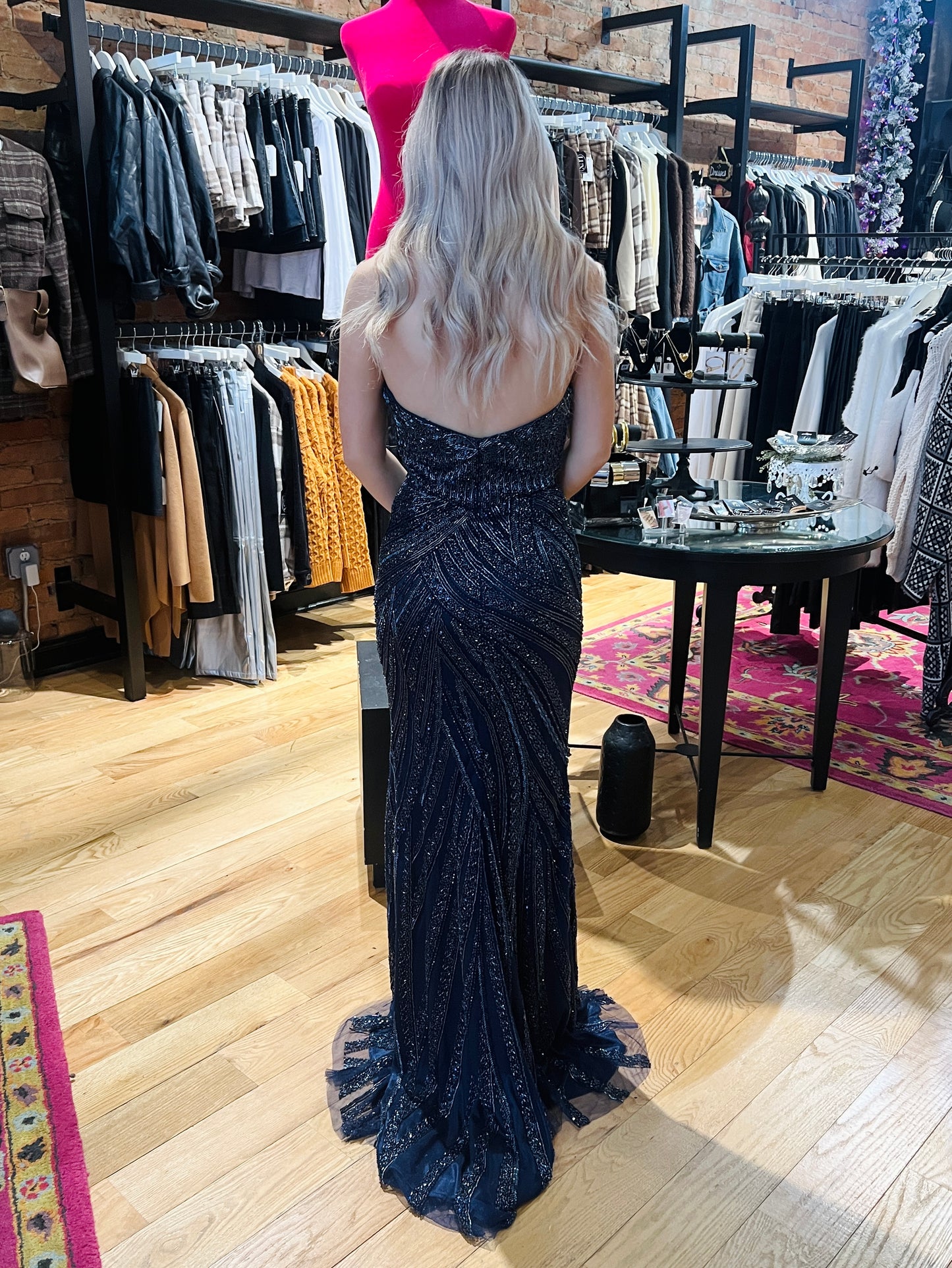 Woman in a dark blue evening gown standing in a clothing store.